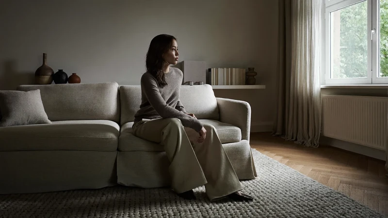 Ruhiges Wohnzimmer in Morgenlicht, neutrales Sofa, Wollteppich und Eichenboden, illustrativ