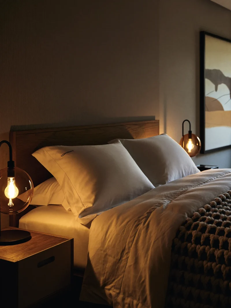 Schlafzimmer mit Leinenbettwäsche, Überwurf und warmen Nachttischlampen, illustrativ